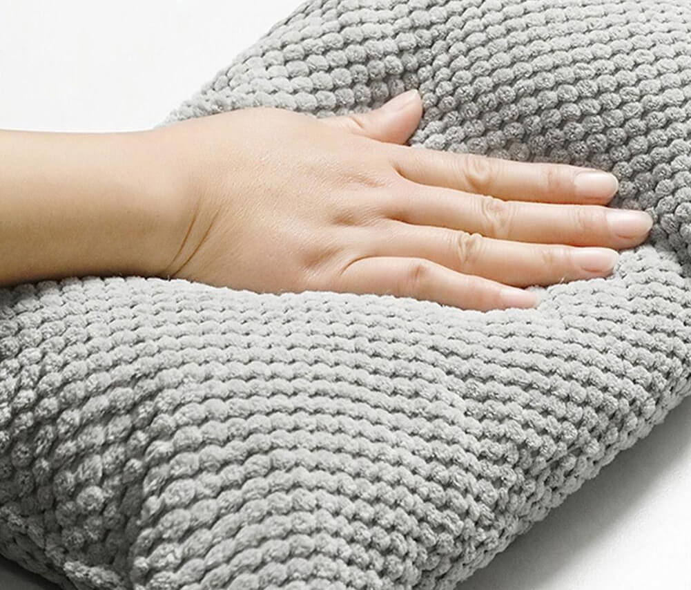 Hand pressing soft, textured gray memory foam pillow; comfortable, ergonomic support for neck and back pain relief. Ideal for restful sleep.