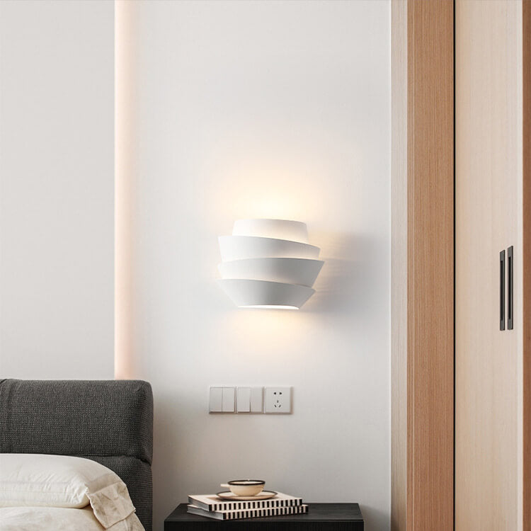 Modern white wall sconce in minimalist bedroom, featuring layered design, soft ambient lighting, and contemporary decor elements.