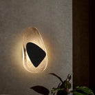 Modern wall sconce with abstract design, featuring a glowing glass fixture and black geometric accent, illuminating a contemporary interior space.