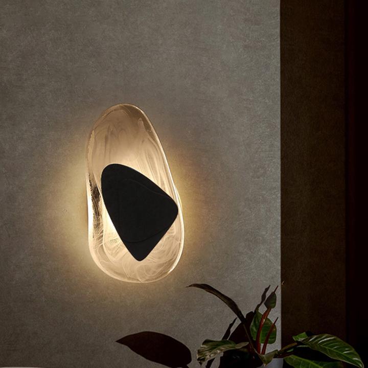 Modern wall sconce with abstract design, featuring a glowing glass fixture and black geometric accent, illuminating a contemporary interior space.