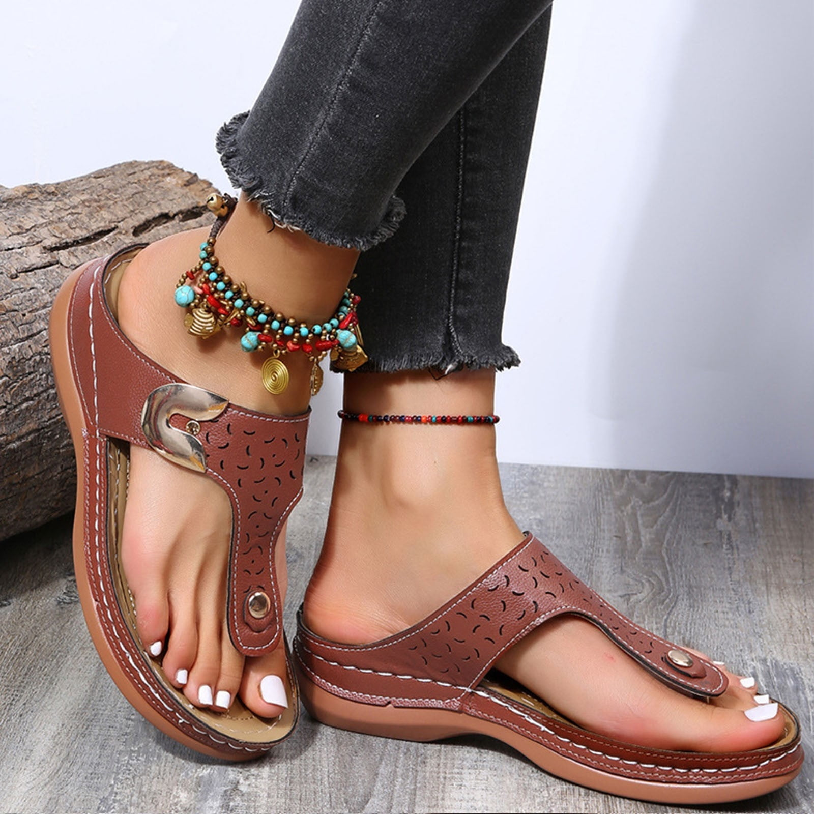 Women's brown leather sandals with cutout design, worn with colorful anklets. Comfortable summer footwear, perfect for casual outfits.