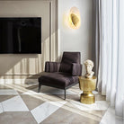 Modern living room with a sleek black armchair, marble floor, gold side table, and decorative bust. Elegant interior design, contemporary decor.