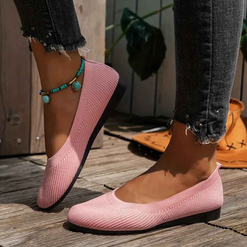 Pink knitted ballet flats on woman's feet, paired with frayed jeans and turquoise anklet, on wooden deck. Stylish casual footwear for women.