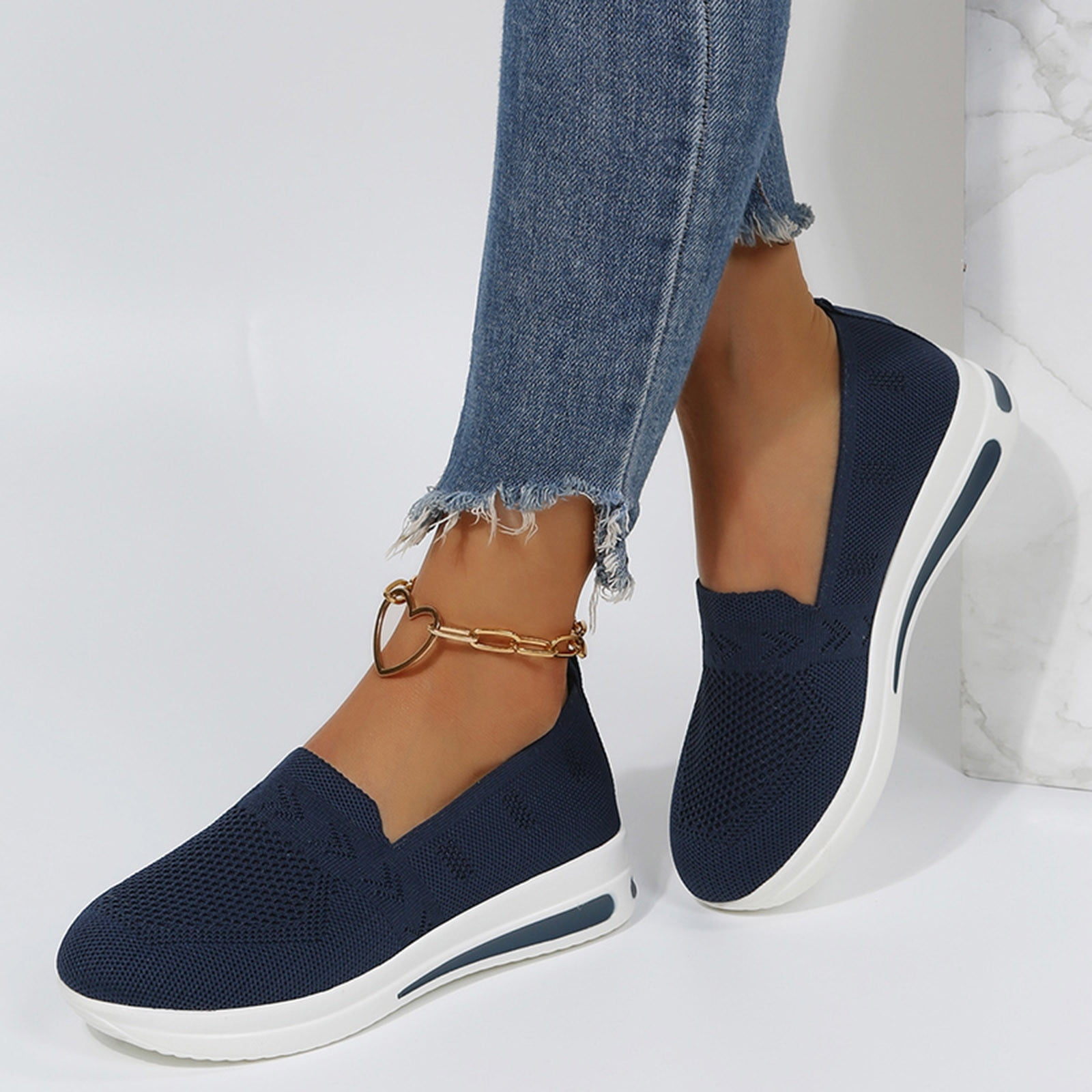 Navy blue slip-on sneakers with white soles, worn with frayed hem jeans and a gold anklet. Stylish women's casual footwear.