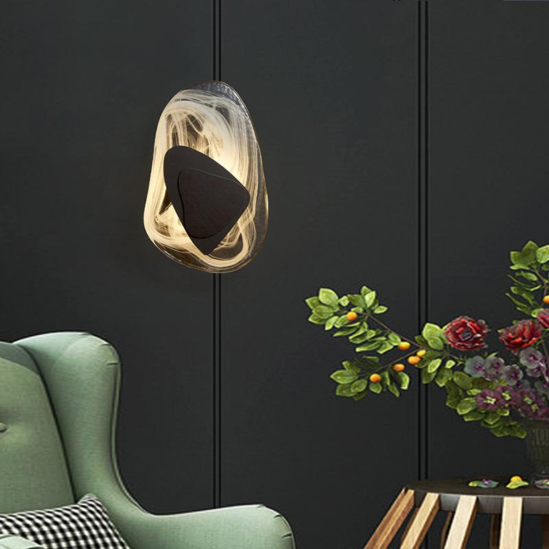 Modern wall sconce with abstract design, featuring a black triangular center and swirling light pattern, mounted on dark panel wall above green armchair.