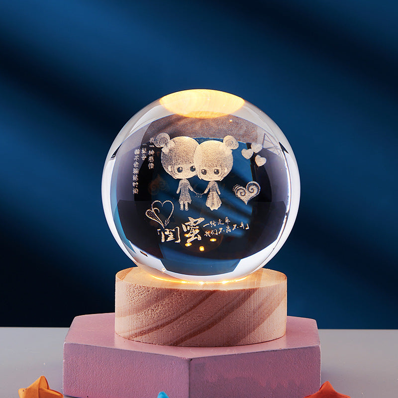 Crystal ball with cute cartoon couple engraving, illuminated on wooden base, against a dark blue background. Perfect for romantic gifts and home decor.