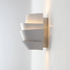 Modern white wall sconce with layered geometric design, mounted on a light-colored wall. Contemporary lighting fixture for home decor.