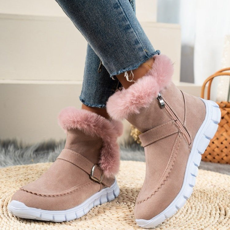 Women's pink suede winter boots with faux fur lining, side zipper, and white rubber soles, paired with blue jeans. Cozy, stylish footwear for cold weather.