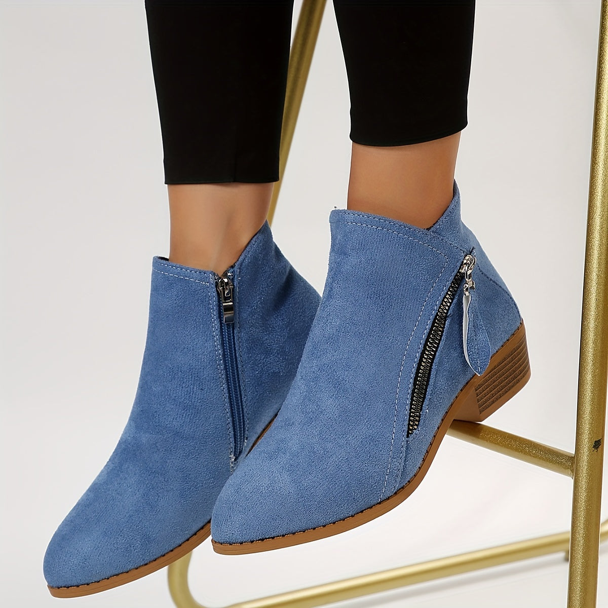 Blue suede ankle boots with side zippers, worn with black leggings. Fashionable women's footwear, perfect for casual and stylish outfits.