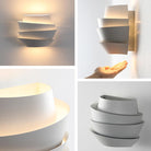 Modern white wall sconce with layered design, emitting soft ambient light. Contemporary home lighting fixture, minimalist decor, energy-efficient.