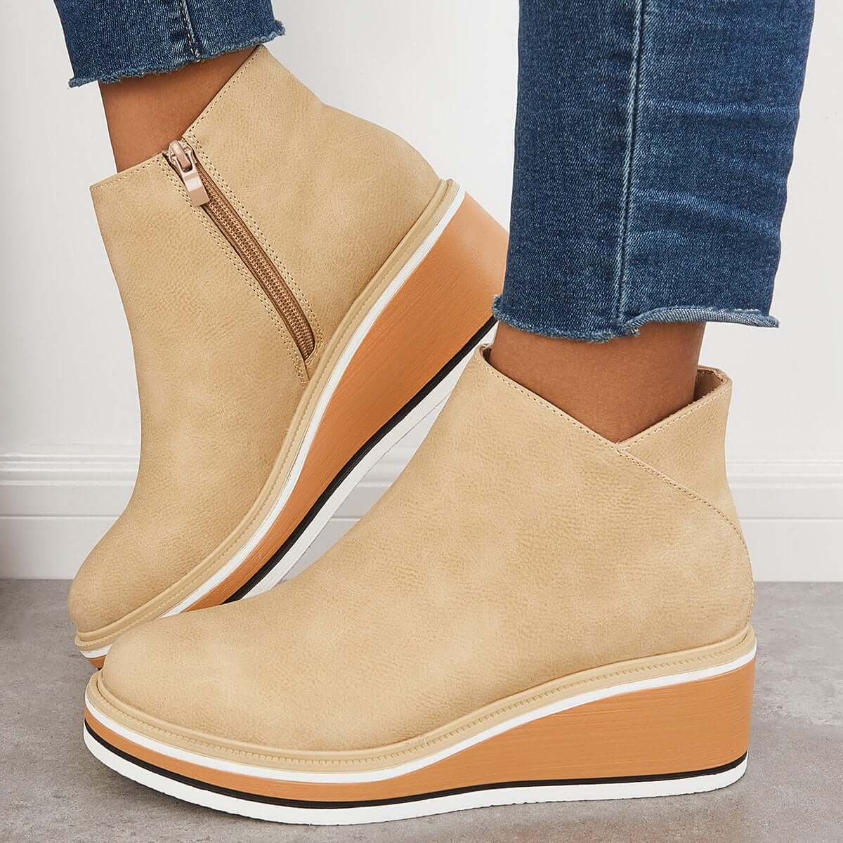 Beige wedge ankle boots with side zipper, worn with blue jeans. Stylish women's footwear, perfect for casual outfits. Fashionable and comfortable design.