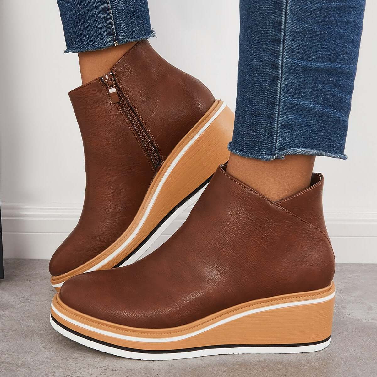 Brown leather wedge ankle boots with side zipper, paired with blue jeans. Stylish women's footwear, perfect for casual and trendy outfits.