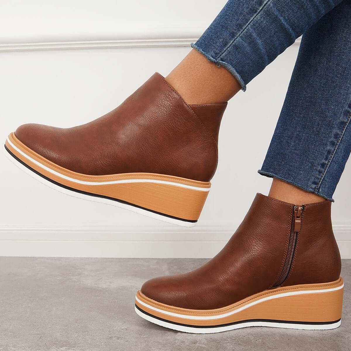 Brown leather wedge ankle boots with side zippers, paired with blue denim jeans. Stylish women's footwear, casual fashion, comfortable design.