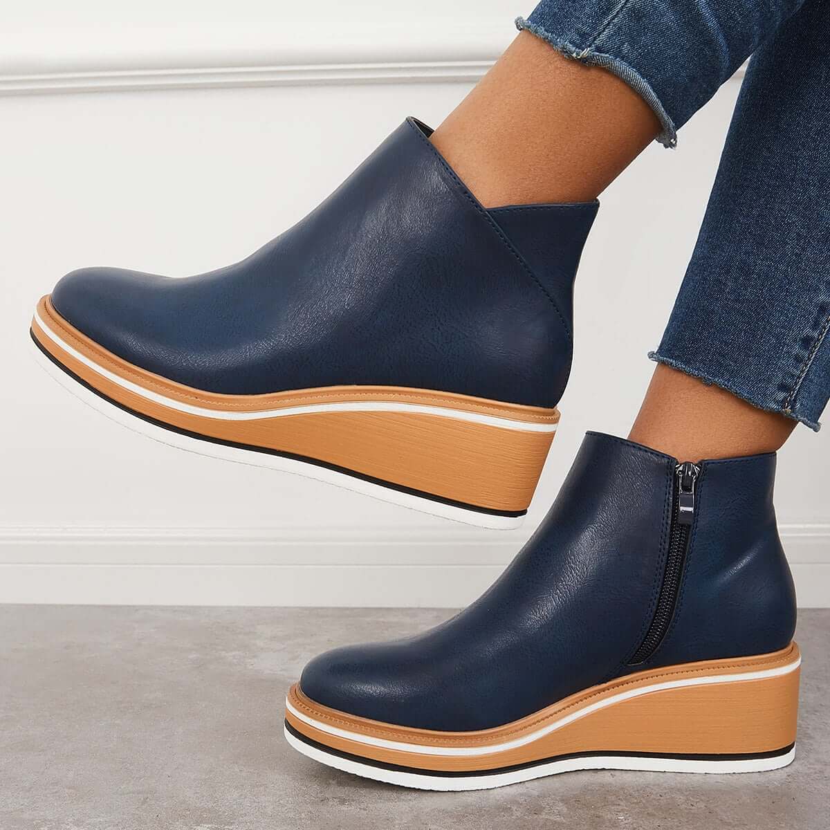 Women's navy blue ankle boots with tan platform soles and side zippers, paired with rolled-up jeans, showcasing trendy fall footwear style.