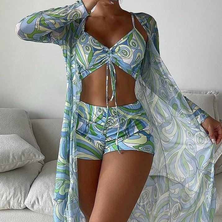 Woman modeling a stylish blue and green abstract print bikini set with matching sheer cover-up, perfect for summer beachwear fashion trends.