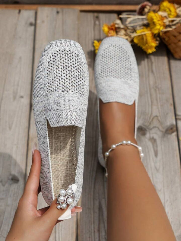 Woman holding stylish white knit slip-on shoes with pearl bracelet, wooden floor background, casual footwear, summer fashion, comfortable loafers.