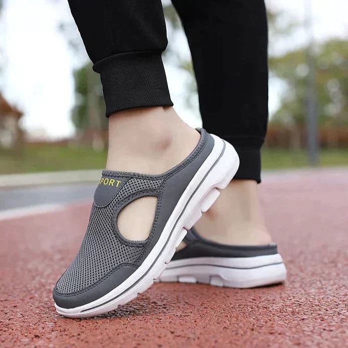 Gray slip-on athletic shoes with breathable mesh upper and cushioned white sole, ideal for walking or casual wear, on a red outdoor track.