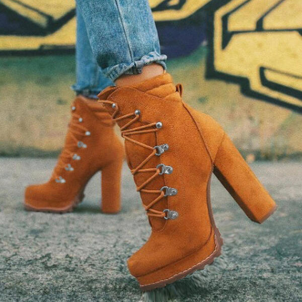 Orange suede high-heeled boots with lace-up design, worn with blue jeans, against a graffiti wall background. Fashionable women's footwear.