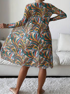 Colorful abstract print dress with long sleeves, featuring swirling patterns in green, orange, and blue, worn by a person standing in a living room.