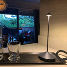 Sleek modern table lamp on a kitchen counter, illuminating a glass and bottle, with a cozy outdoor patio view in the background.