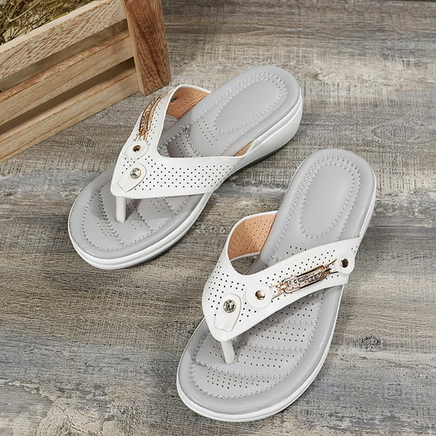 White leather women's sandals with perforated design and cushioned soles on a wooden floor. Stylish summer footwear, comfortable and trendy.