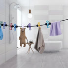 Modern bathroom with freestanding bathtub, rain shower, and towels hanging on a line with colorful clothespins. Minimalist decor, bright lighting.