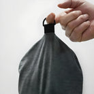 Hand holding a gray microfiber towel by a black loop against a white background. Ideal for cleaning, quick-drying, and travel use.