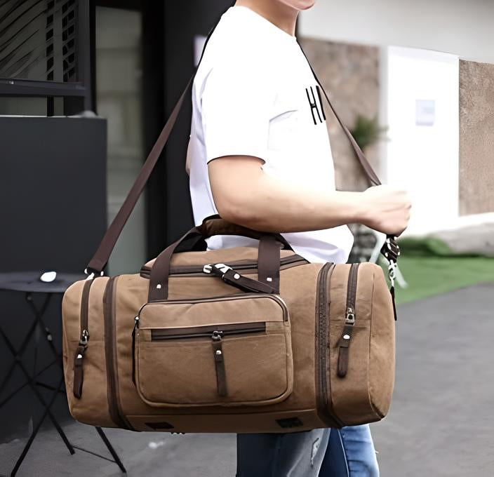 Man carrying a stylish brown canvas duffel bag with multiple zippered compartments, ideal for travel and gym use, wearing casual attire.