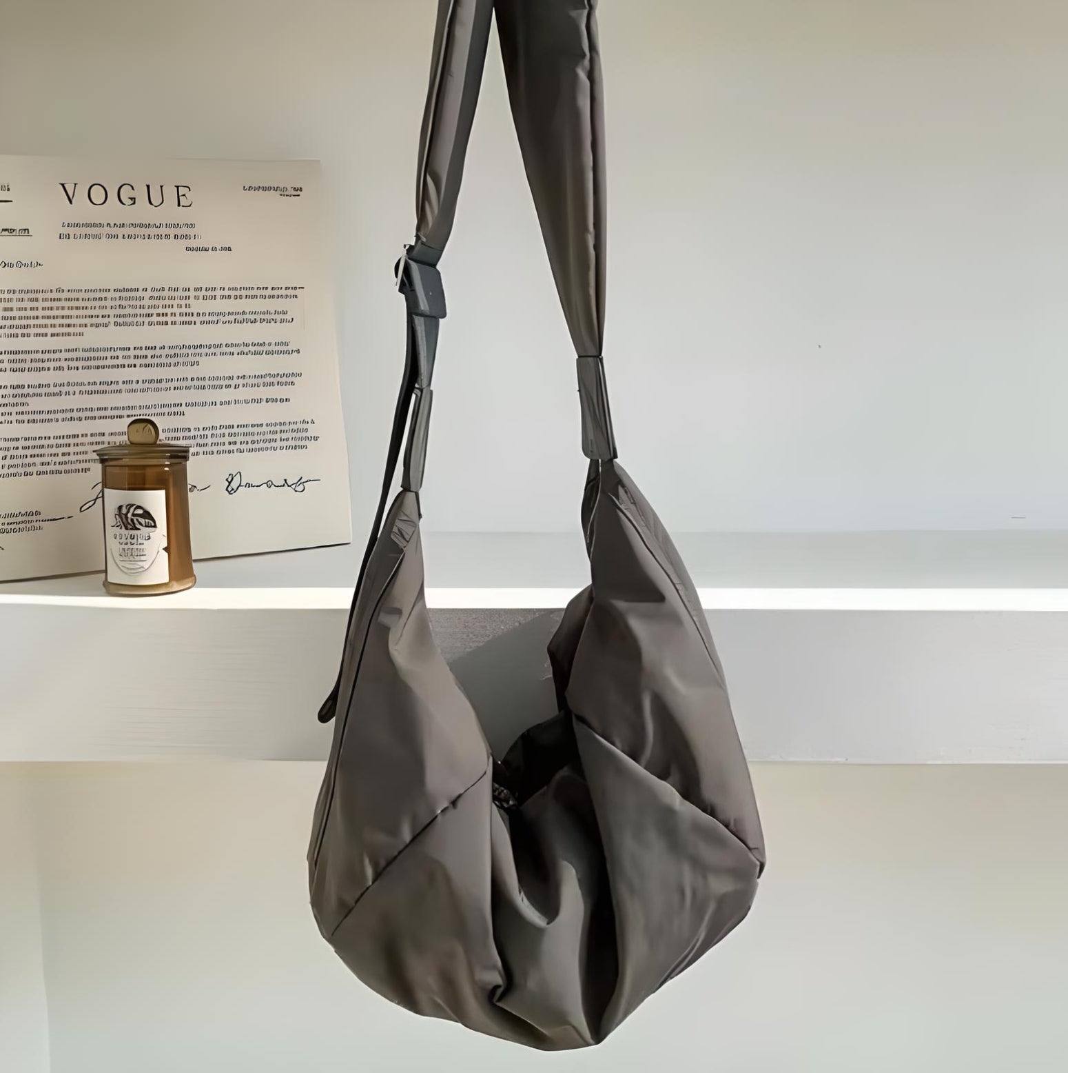 Stylish gray hobo bag on display shelf with Vogue magazine and candle; modern fashion accessory, minimalist design, chic handbag for women.