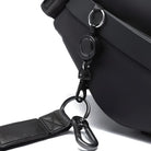 Close-up of a black leather bag with a detachable strap and metal carabiner clip, showcasing durable hardware and sleek design. Perfect for travel or daily use.