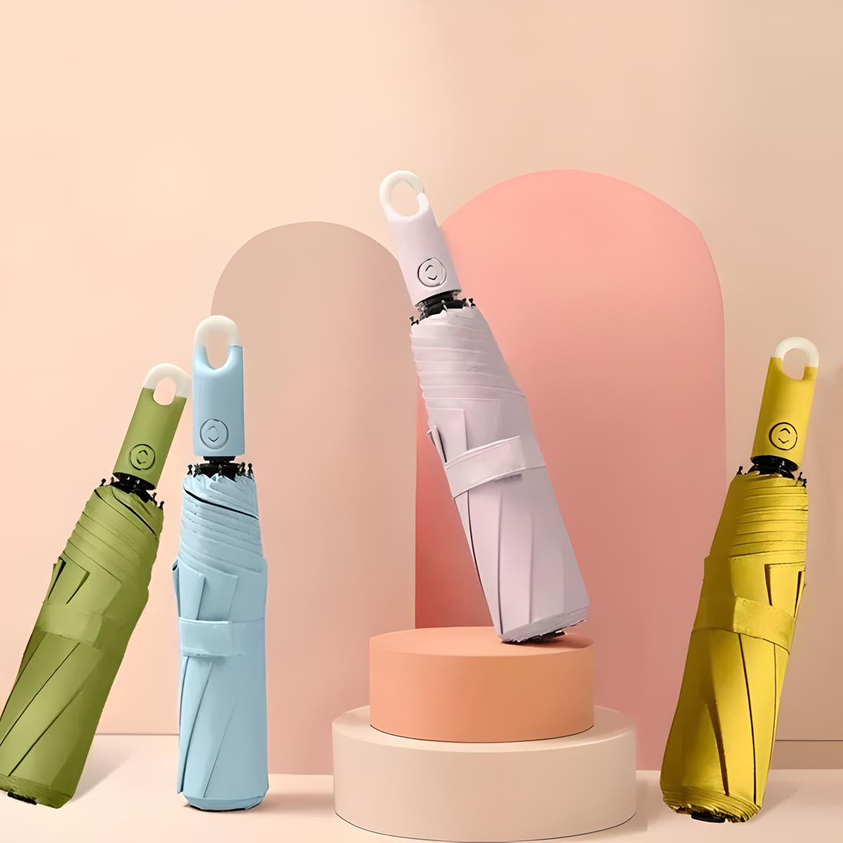 Colorful compact umbrellas with ergonomic handles displayed on pastel geometric podiums, featuring green, blue, white, and yellow designs.