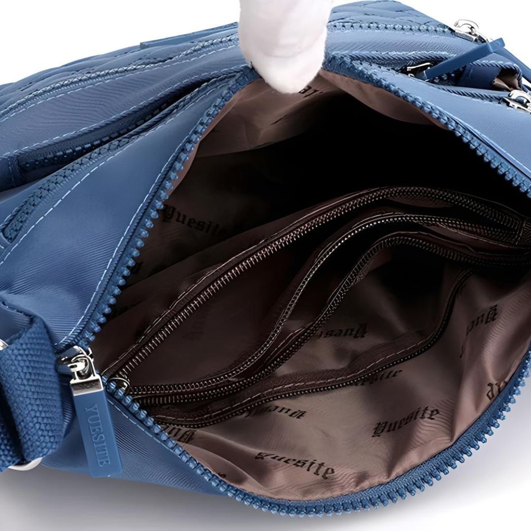 Blue crossbody bag with multiple zippered compartments, open to reveal spacious interior and branded lining. Ideal for travel and everyday use.