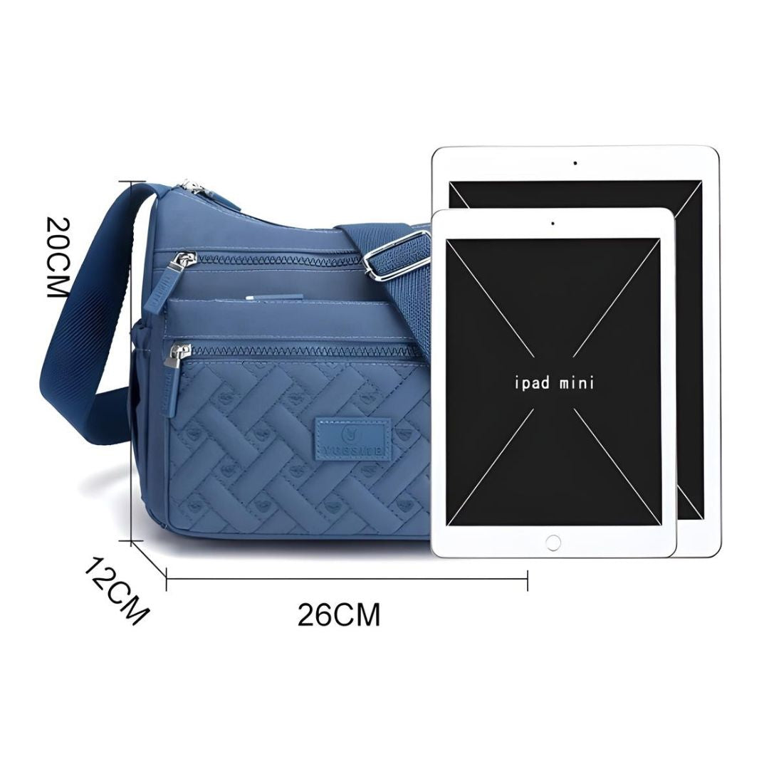 Blue crossbody bag with adjustable strap, multiple zippered compartments, and iPad Mini for size comparison. Stylish, practical, and spacious design.