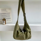 Olive green hobo bag with adjustable strap on white shelf, next to a Vogue magazine and a candle. Stylish, versatile fashion accessory.