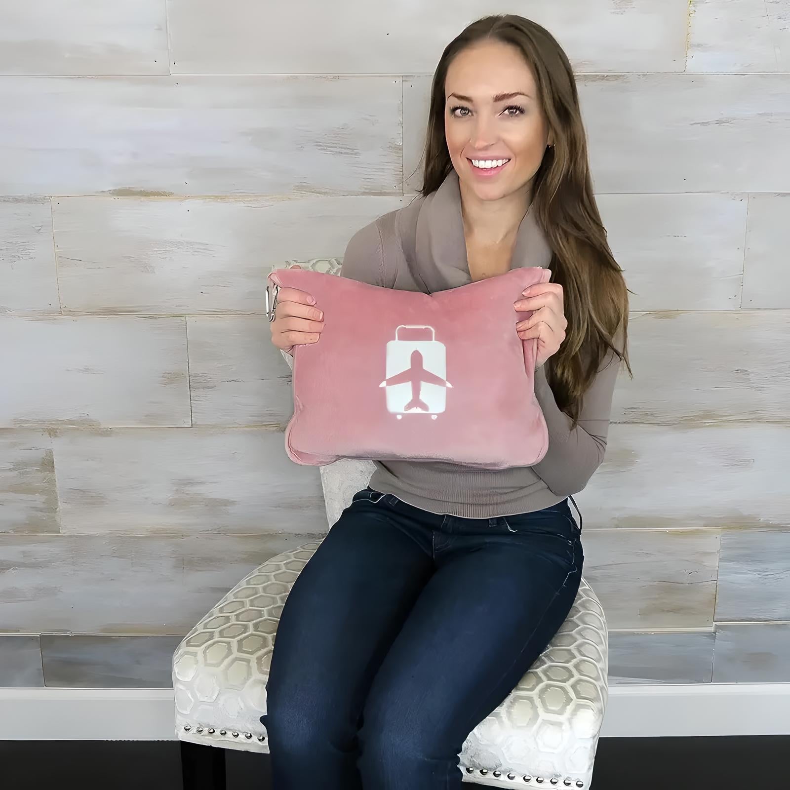 Woman holding pink travel pillow with airplane logo, sitting on a patterned chair against a wooden wall. Travel accessory, comfort, relaxation.