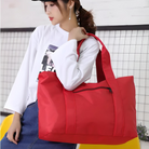 Woman holding large red tote bag with zipper, wearing white long-sleeve shirt and denim skirt. Fashionable, spacious handbag for casual outings.