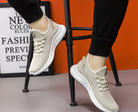 Beige athletic sneakers with white soles on a person sitting, showcasing breathable mesh design and lace-up closure, ideal for running and casual wear.