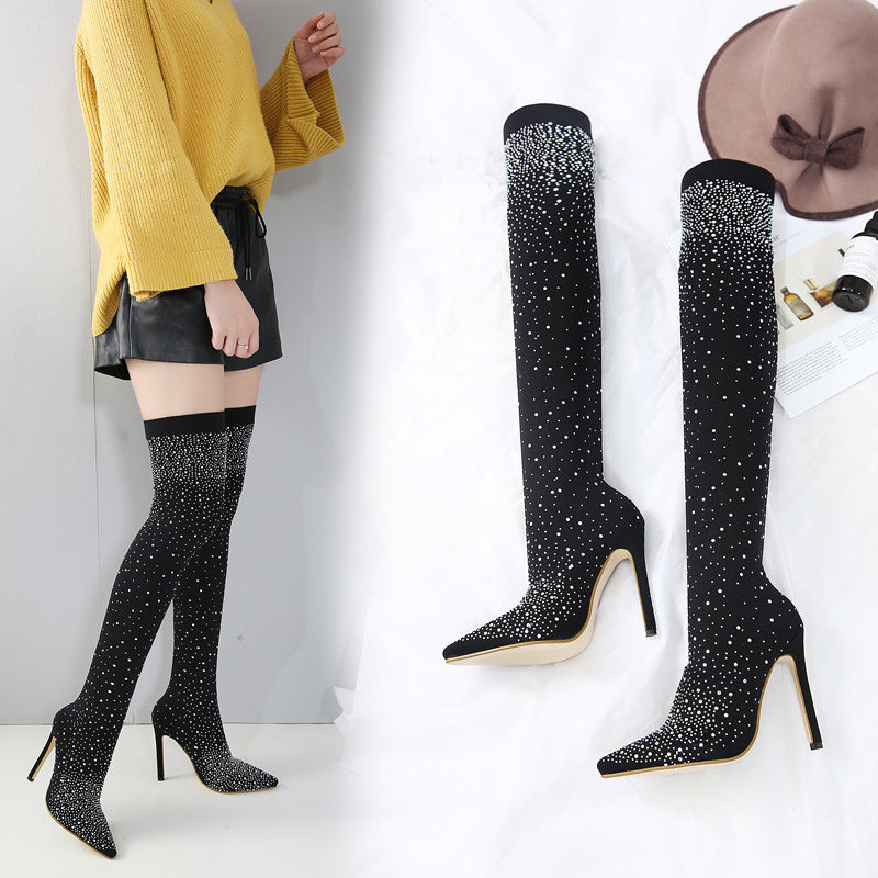 Black rhinestone thigh-high stiletto boots with pointed toes, paired with a yellow sweater and black leather shorts. Fashionable women's footwear.