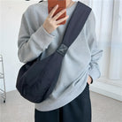 Person wearing a gray sweatshirt and black crossbody bag, holding a smartphone. Casual fashion, modern style, comfortable outfit, indoor setting.