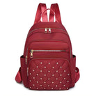 Red quilted backpack with studded front pocket, multiple zippered compartments, and adjustable straps. Stylish women's fashion accessory.