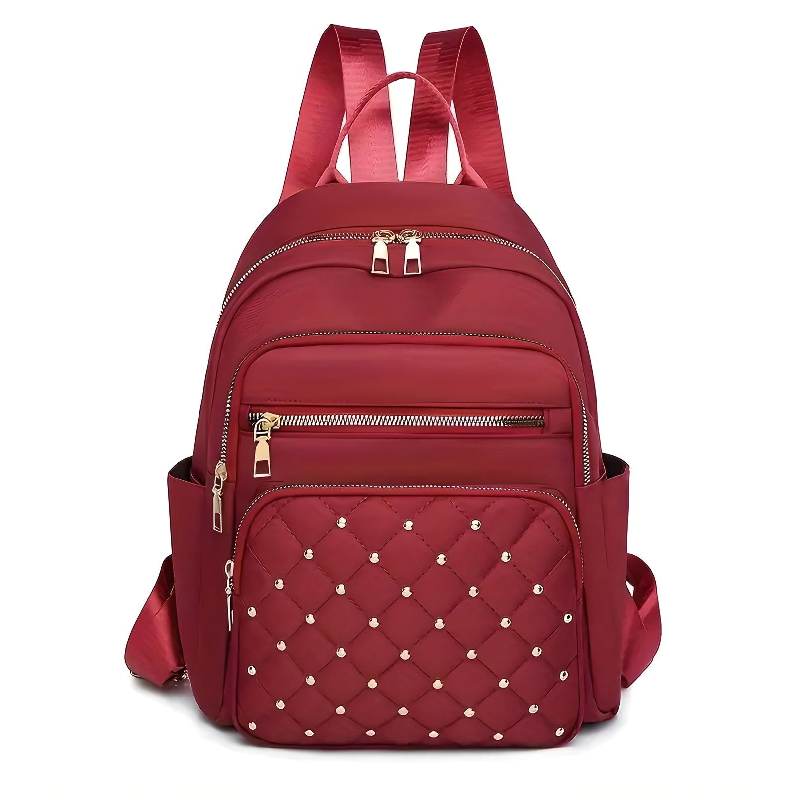 Red quilted backpack with studded front pocket, multiple zippered compartments, and adjustable straps. Stylish women's fashion accessory.