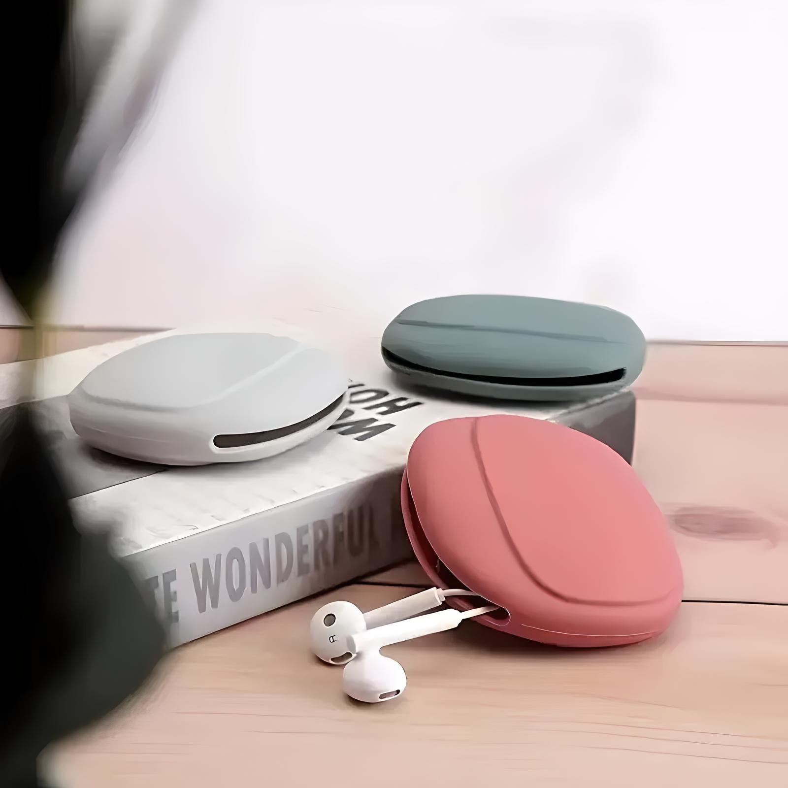 Round silicone earbud cases in pink, gray, and green on a wooden surface with earbuds. Stylish earphone storage, portable accessory organizer.