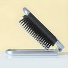 Folding hairbrush with black bristles and silver handle on a light background. Compact travel hairbrush, portable grooming accessory.