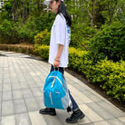 Young person walking on a tiled path with a blue and white backpack, wearing a white cap, oversized t-shirt, and black boots, surrounded by greenery.