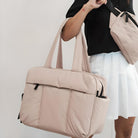 Woman holding a stylish beige tote bag with black accents, wearing a black top and white skirt. Perfect for fashion-forward, versatile everyday use.