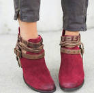 Red suede ankle boots with brown leather straps and buckles, worn with gray jeans. Stylish women's footwear, perfect for casual fashion.