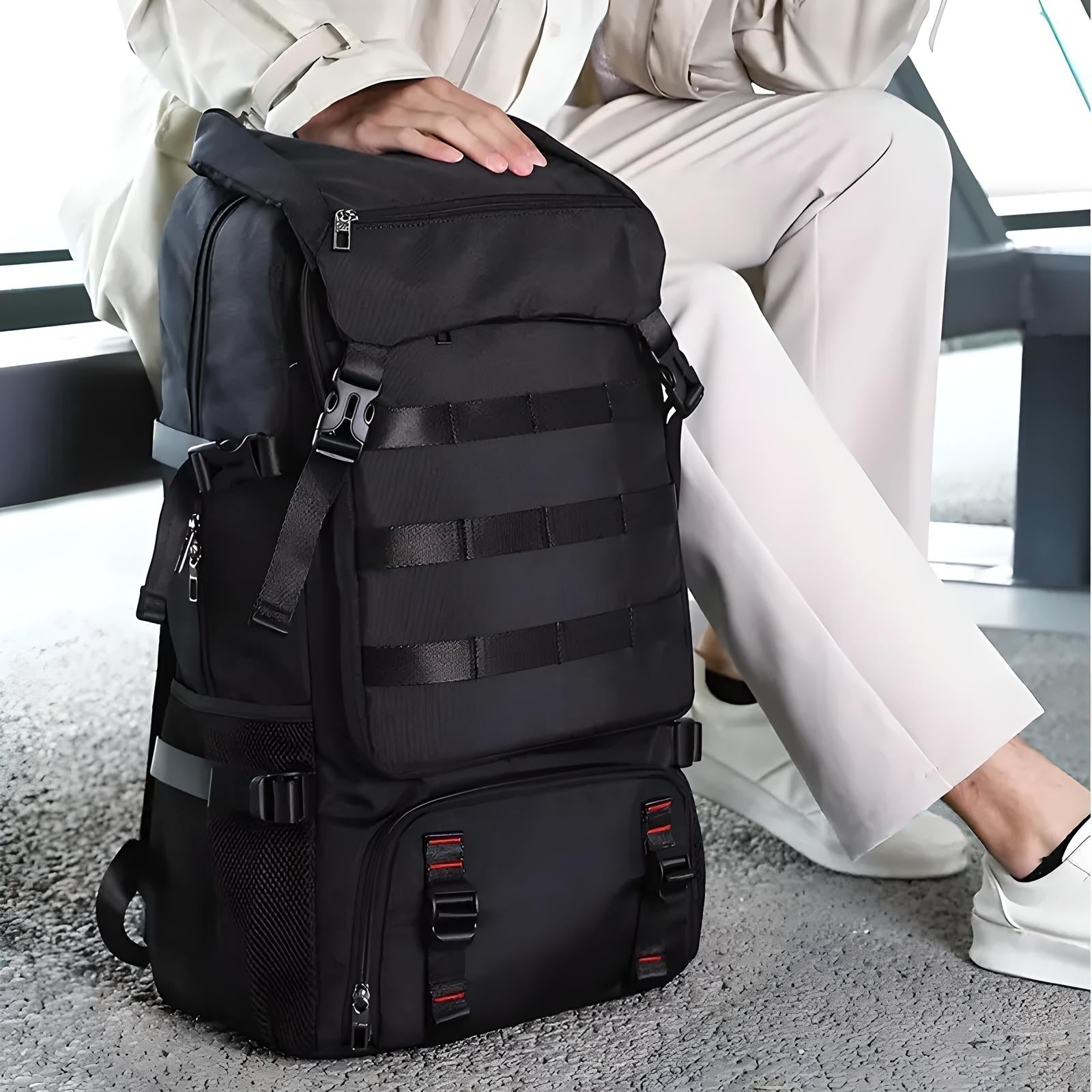 Black tactical backpack with multiple compartments and straps, ideal for travel and outdoor activities, showcased on a seated person in casual attire.