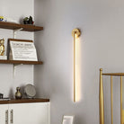 Modern gold wall sconce light fixture in a stylish living room with wooden shelves, decorative items, and a minimalist design. Perfect for home decor.