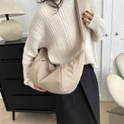 Woman in cozy white sweater holding a beige oversized shoulder bag, standing in a modern room with black dresser and white lamp. Fashionable winter outfit.