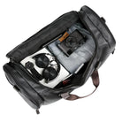 Open black leather duffel bag with camera, headphones, watch, jeans, and notebook inside. Perfect travel essentials for stylish, organized packing.